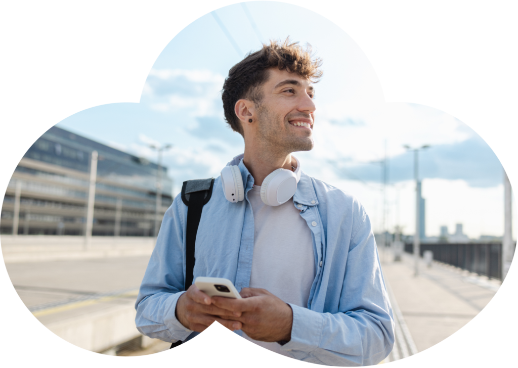 Young man with headphones smiling at his phone outdoors